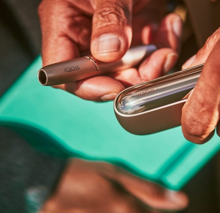 Rokas tur IQOS ILUMA ierīci Golden Khaki krāsā